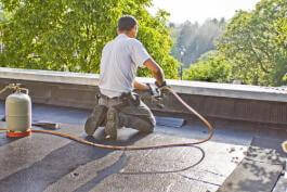 גגן עם מבער גז כורע על גג, ומחמם חתיכת קירוי רגישה.